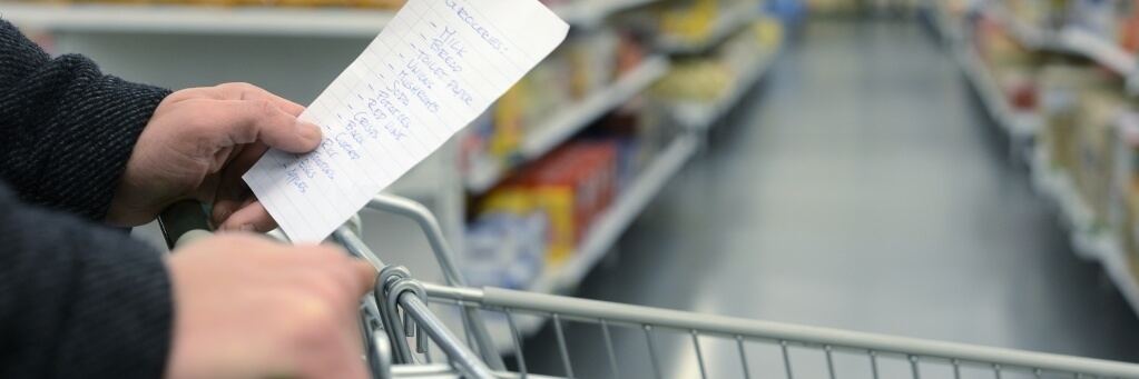 Close up of hands of a person holding a grocery list and pushing grocery cart through the store.