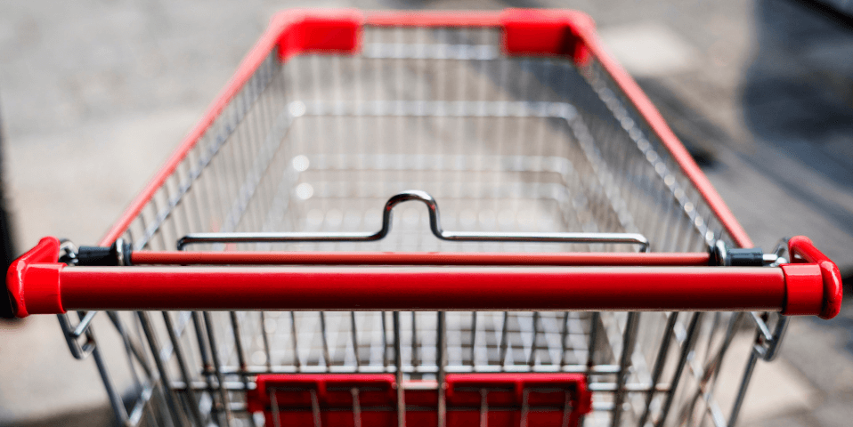 An empty wire shopping cart with red plastic handle and accents.