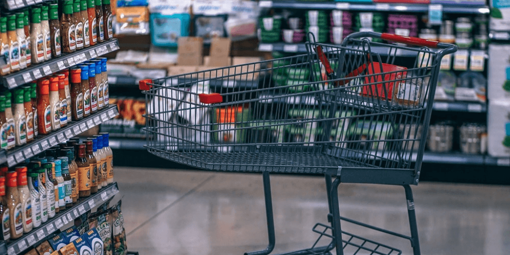 An empty grocery shopping cart sits in the salad dressing aisle at the grocery store.